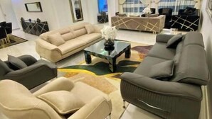 Ein modernes Wohnzimmer mit einem beigefarbenen Sofa, einem dunkelgrauen Sofa und einem Couchtisch. Im Hintergrund befindet sich ein Fernseher und ein Fenster mit Vorhängen.