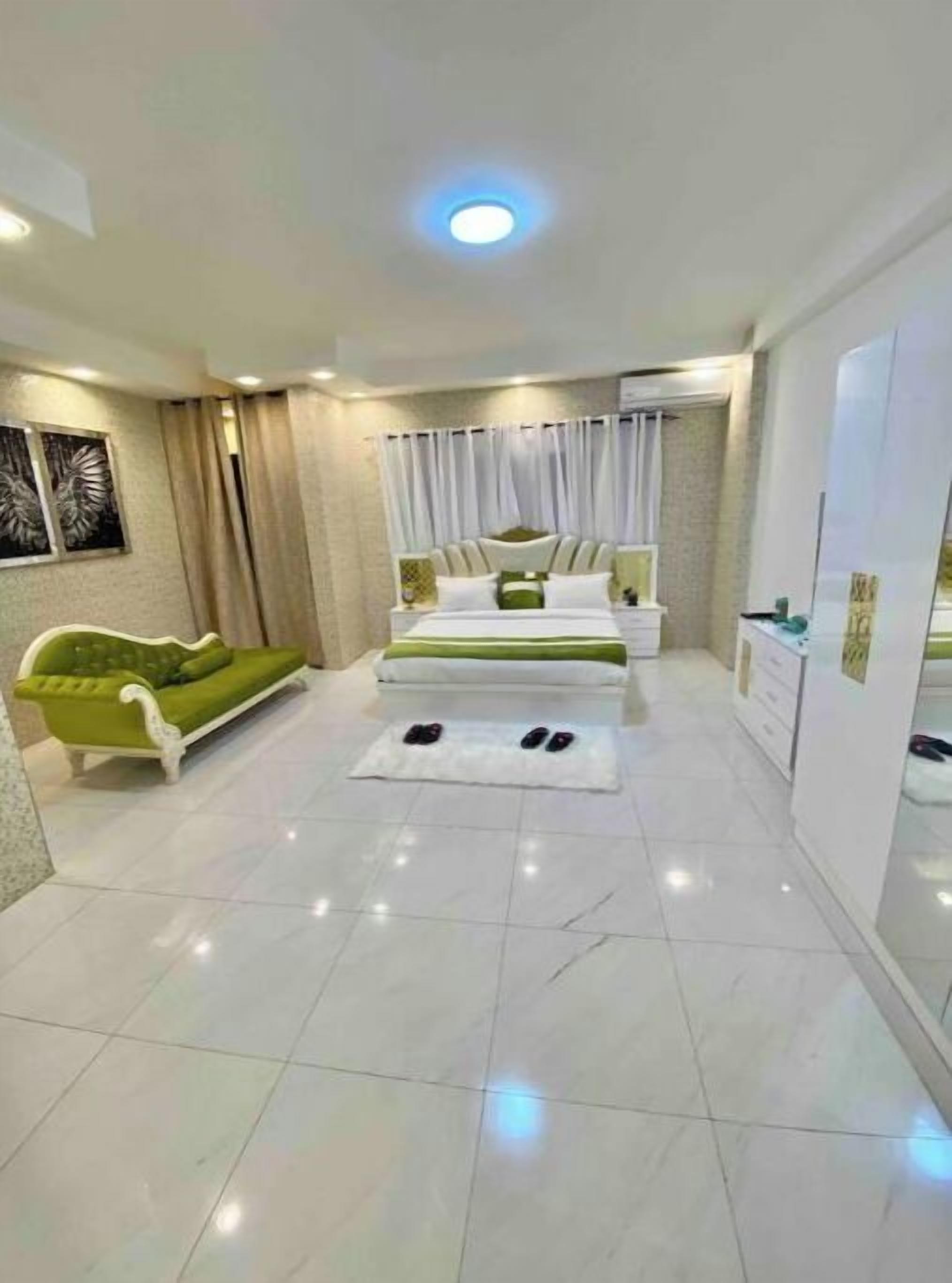A modern bedroom with a bed, a green sofa, and a white dresser.