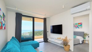 A modern living room with a large sofa, a flat-screen TV, and a balcony with a view of the city. - Hedera A40 (Dubrovnik)