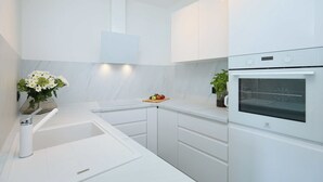 A modern kitchen with white cabinetry, a built-in oven, and a small countertop with a fruit bowl and potted plants. - Hedera A40 (Dubrovnik)