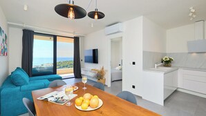 A modern living room with a wooden dining table, a teal sofa, and a large window with a view of the sea. - Hedera A40 (Dubrovnik)