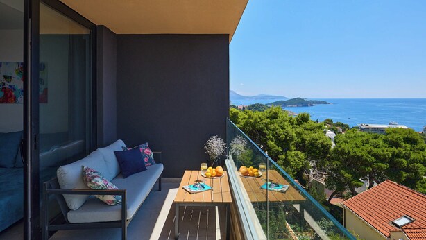 A balcony with a sofa, a table with fruit and drinks, and a view of the sea and greenery. - Hedera A40 (Dubrovnik)
