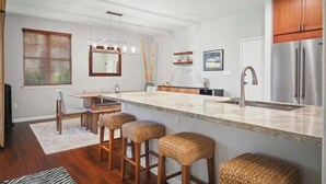 Une cuisine moderne dotée d’un grand îlot central, d’appareils électroménagers en acier inoxydable et d’un coin repas avec des tabourets de bar.