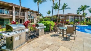 Un espace aménagé au bord de la piscine, comprenant des barbecues d’extérieur, une table et des chaises.
