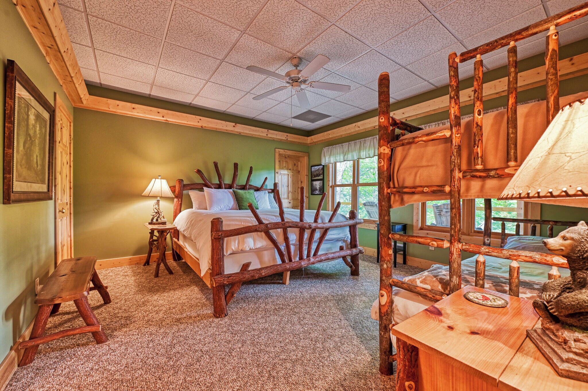 Une chambre à coucher rustique avec un cadre de lit en bois, un ventilateur de plafond, un banc en bois et une statue d’ours.
