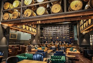 A bar with wooden barrels, leather seating, and a wall of liquor bottles.