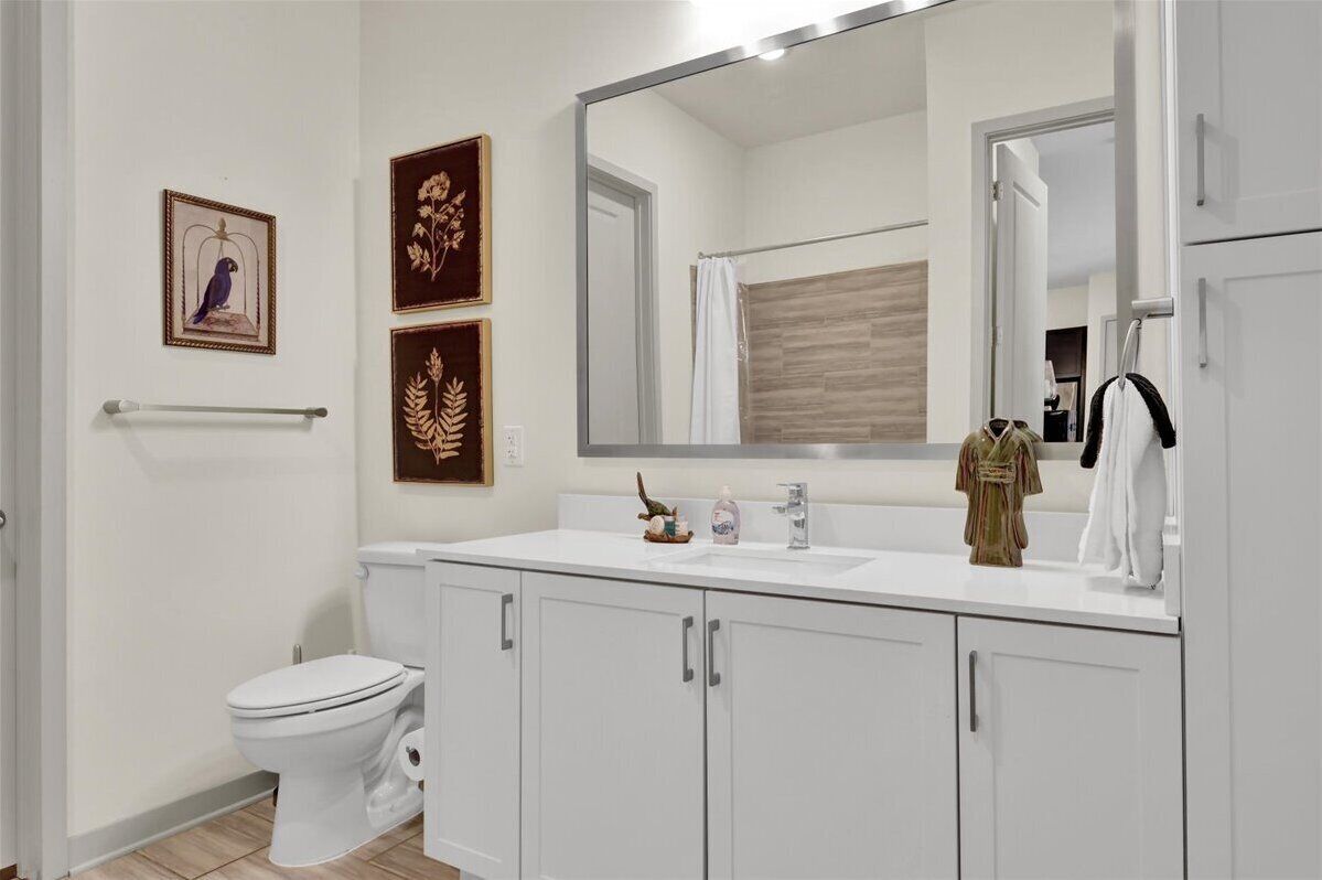Een moderne badkamer met een wit toilet, een grote spiegel en een witte wastafel met een handdoek erboven.