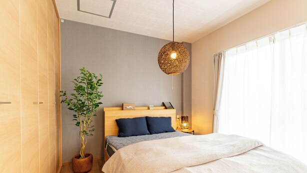 Quarto com cabeceira de madeira, cama grande com colcha listrada, planta em vaso, luminária pendente e mesa de cabeceira com abajur.