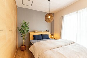 A bedroom with a wooden headboard, a large bed with a striped bedspread, a potted plant, a hanging light fixture, and a nightstand with a lamp.