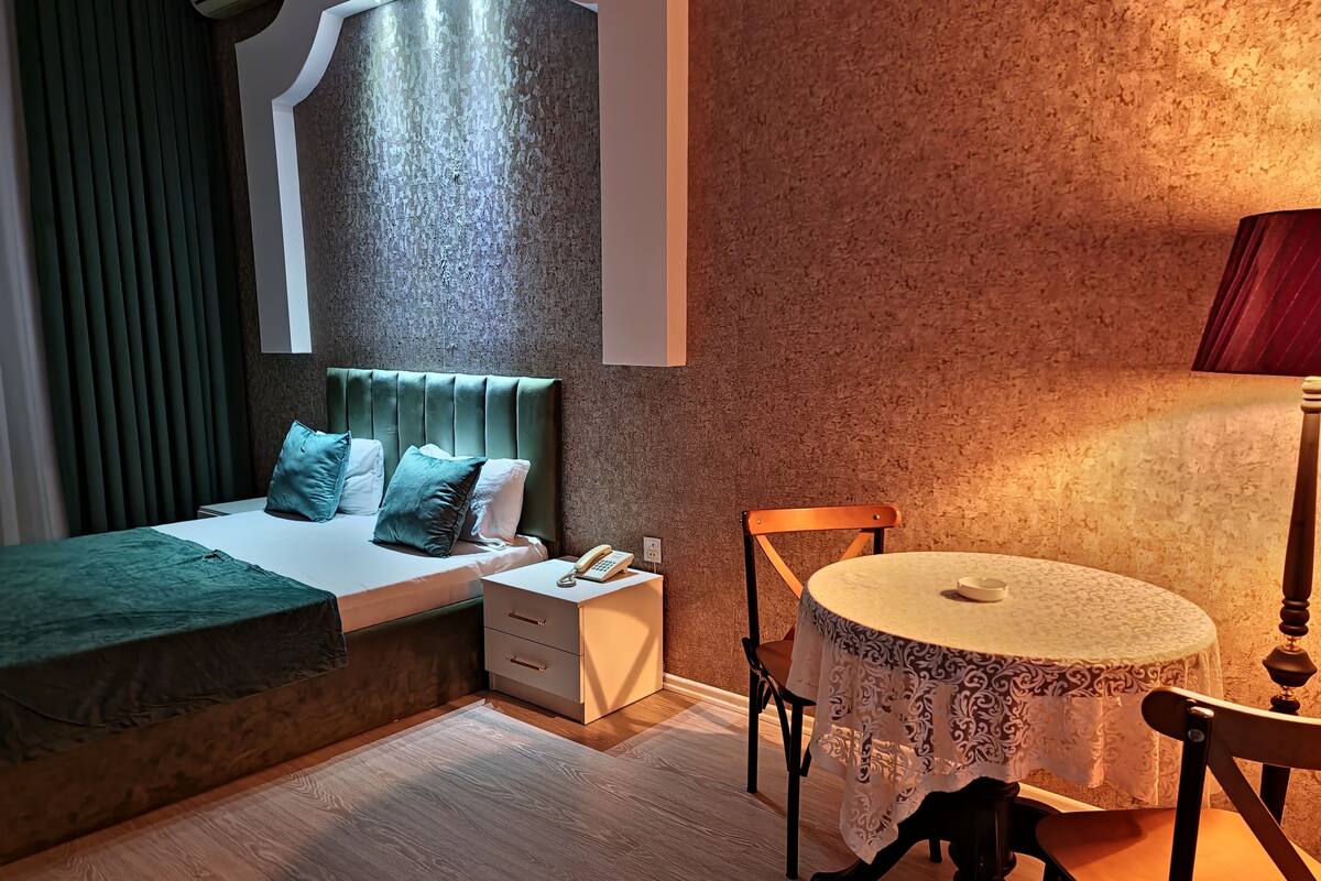 A bedroom with a bed, bedside table, lamp, and a small round table with a chair.