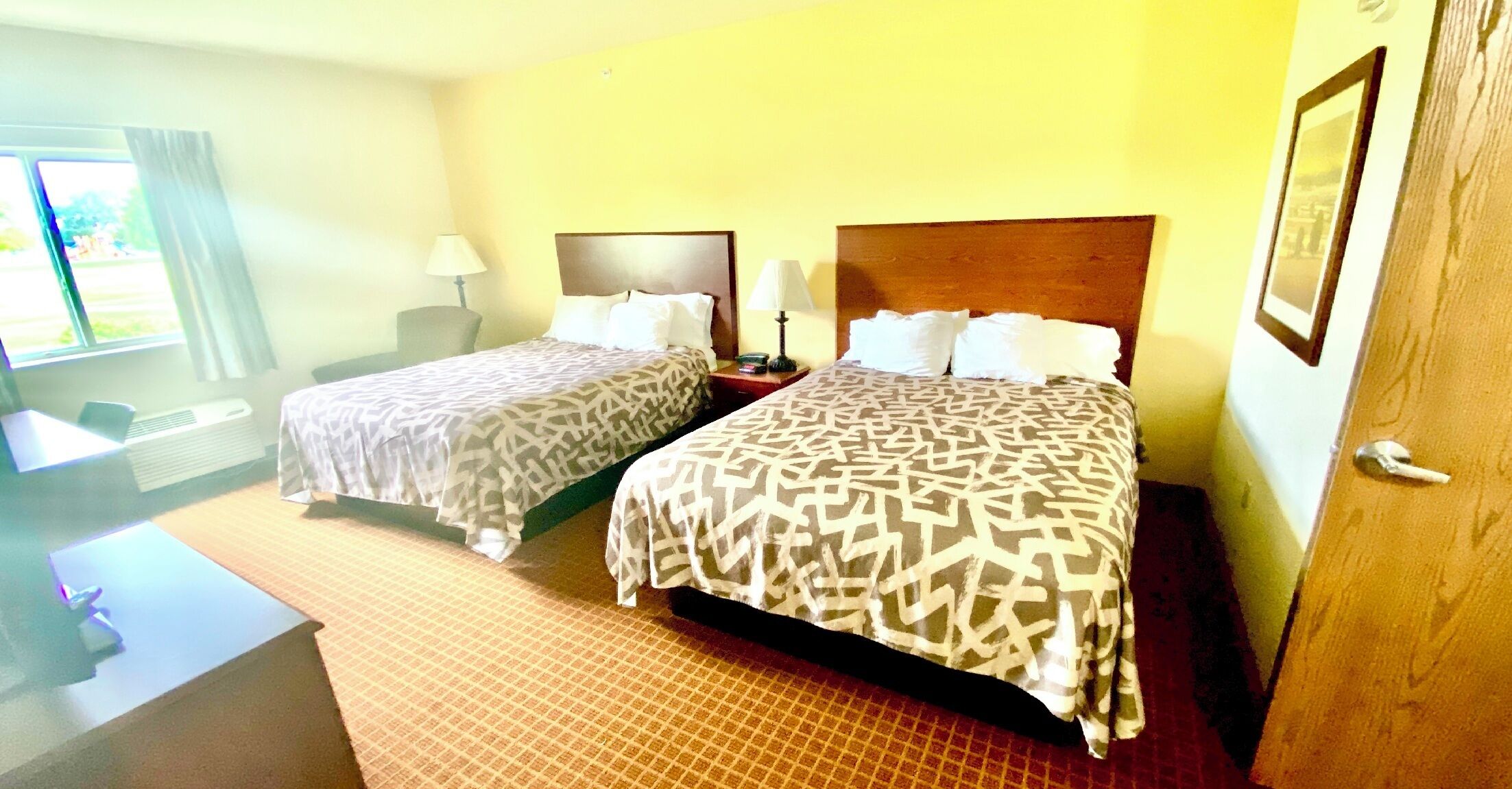 A hotel room with two beds, a desk, a chair, and a window.