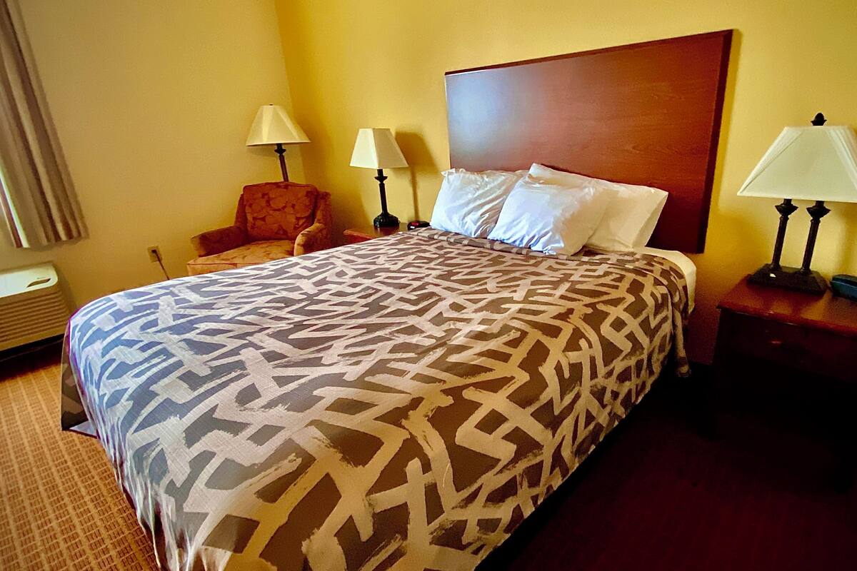 A hotel room with a large bed, two bedside lamps, a wooden headboard, and a chair.