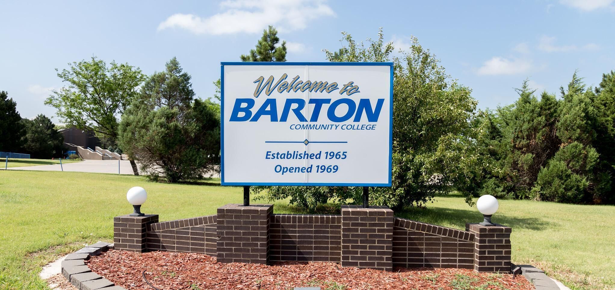 Letrero de bienvenida del Barton Community College, con un cielo despejado y follaje en el fondo.