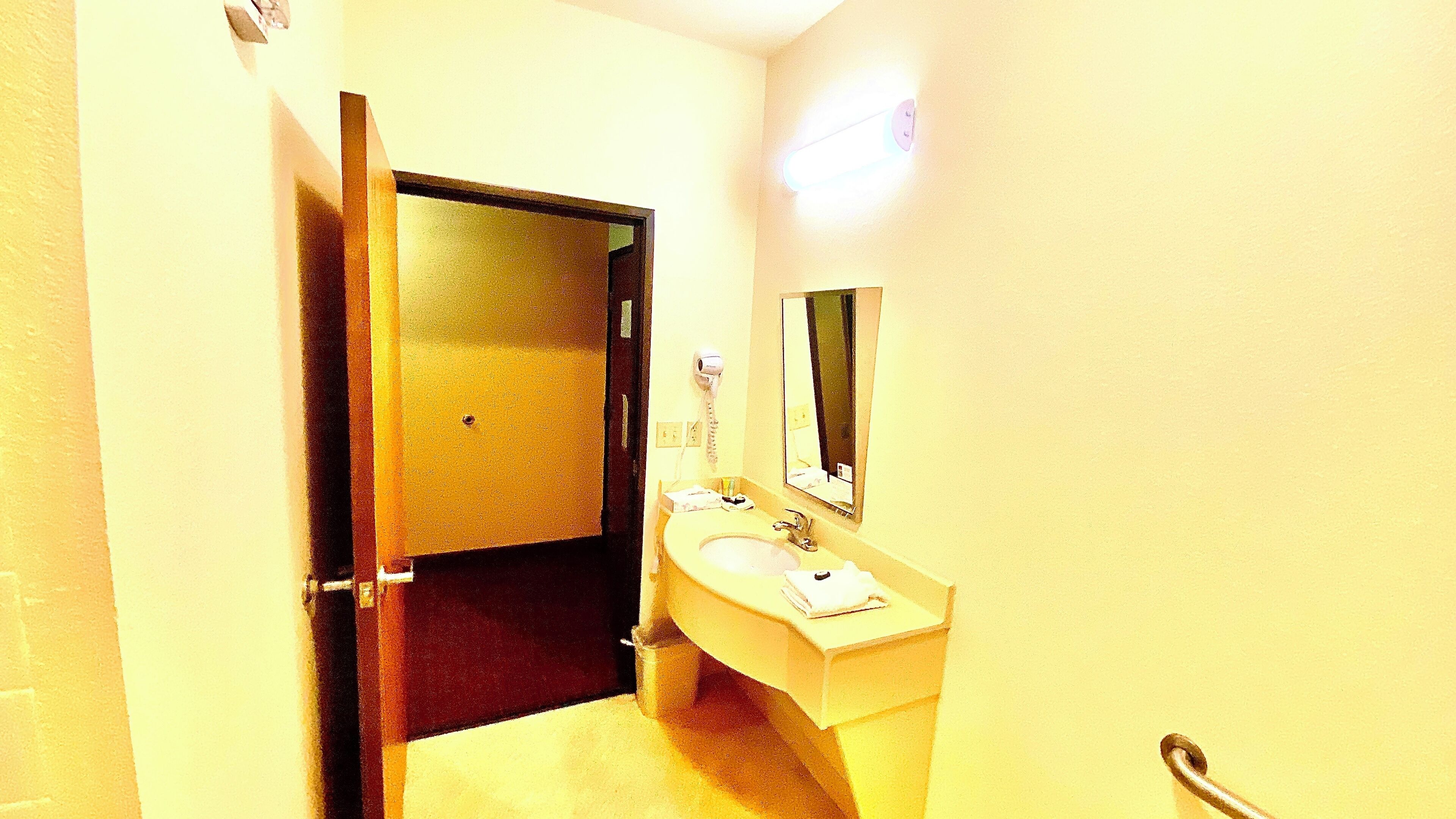 A hotel bathroom with a sink, mirror, and a door leading to another room.