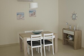 A dining area with a wooden table, white chairs, a bowl, and a small wooden cabinet with a mirror and decorative items. - Marvelous T1 apartment - Cabanas de Tavira (Tavira)