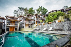 A pool area with a clear blue pool, lounge chairs, and a stone wall with potted plants. - Tree House Lodge (Nusa Dua)