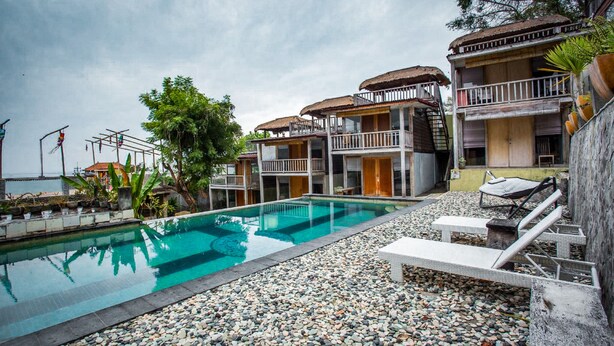 Un área de piscina con un deck de piedra, sillas de descanso y un edificio con balcones.