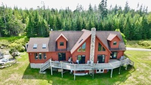 A large, two-story house with a wrap-around porch, surrounded by a well-maintained lawn and dense forest. - Cabin on the Ocean-Carvers Cove (Vinalhaven)