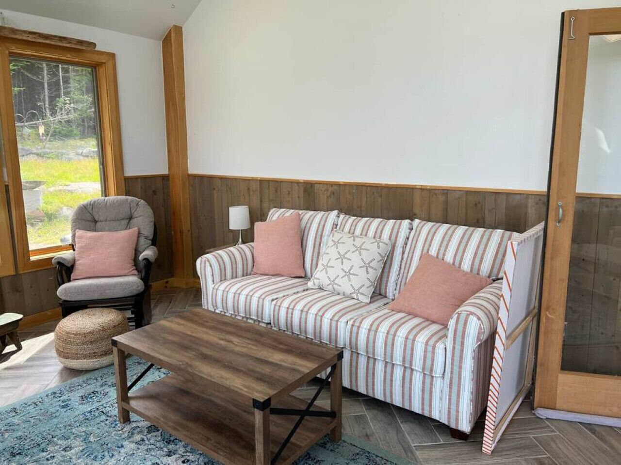 A cozy living room with a striped sofa, a wooden coffee table, a grey armchair, and a small ottoman.