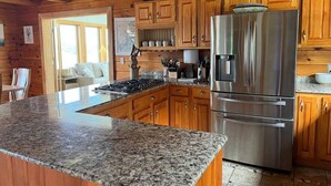 A kitchen with granite countertops, stainless steel appliances, wooden cabinets, and a large island. - Cabin on the Ocean-Carvers Cove (Vinalhaven)
