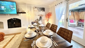 A dining area with a wooden table set for four, a fireplace, and a television mounted on the wall.