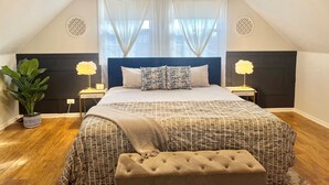 A bedroom with a large bed, two bedside tables, a nightstand, a potted plant, and a hanging light fixture.