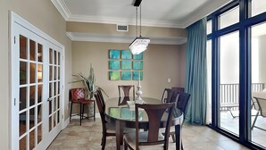 Een eetgedeelte met een ronde tafel, zes stoelen en een kroonluchter. Er hangen zes kunstwerken in blauwgroen aan de muur.