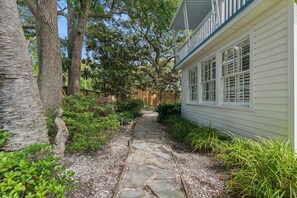 A stone pathway leading to a house with a porch, surrounded by trees and greenery.