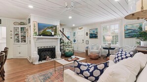 A living room with a fireplace, a television, and a staircase leading to another level. - Nostalgia of 1930’s with modern kitchen and baths, sleeps 8 (St Simons Island)