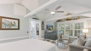 A bedroom with a large bed, a ceiling fan, a dresser, a chair, and a window with blinds. - Nostalgia of 1930’s with modern kitchen and baths, sleeps 8 (St Simons Island)