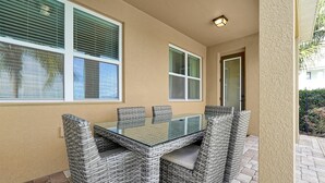An outdoor patio with a glass-top table and wicker chairs, beige walls, and a door leading to the interior. - Reunion Encore Resort Villa W/ Pool Spa Gameroom (kissimmee)