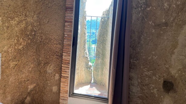 Una stretta finestra ad arco con vista su un paesaggio montuoso.