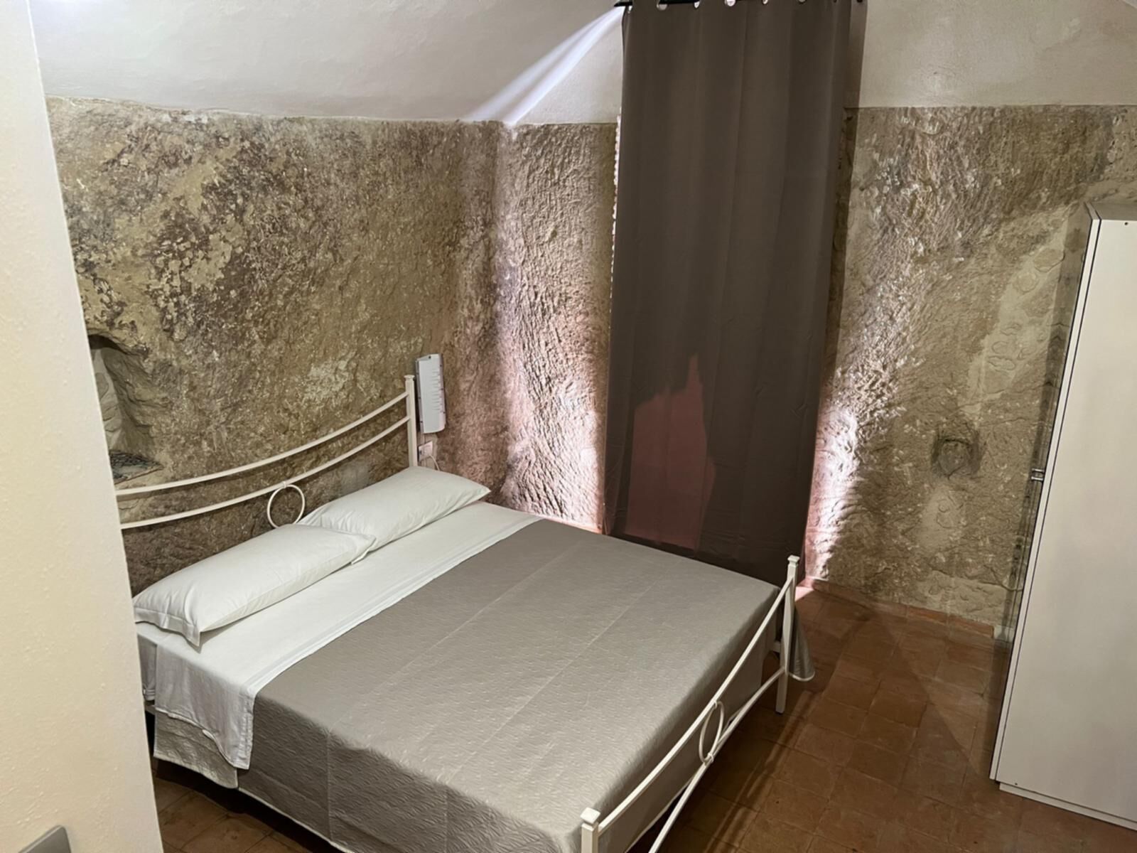 A single bed with a metal frame, white bedding, and a wall-mounted light fixture.