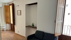Un soggiorno con un divano blu scuro, un mobile in legno, una piccola pianta su uno scaffale e una sedia bianca.