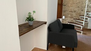 Un soggiorno con un divano scuro, una mensola in legno con una pianta in vaso, una scala e una parete in pietra.