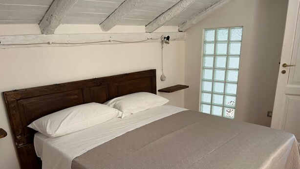 Una camera da letto con una testiera in legno, un letto con biancheria da letto bianca, una piccola finestra e una porta.