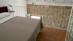 A bedroom with a bed, a stone wall, and a balcony with a railing. - Three Bedroom Apartment (TROPEA)