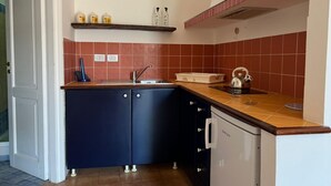 A compact kitchen with dark blue cabinets, a white refrigerator, and a tiled backsplash. - Three Bedroom Apartment (TROPEA)