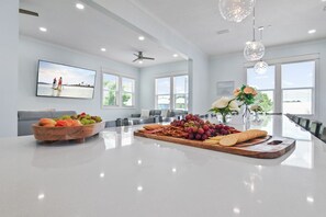 A modern kitchen with a large island, a dining area with a long table, and a view of the outdoors.