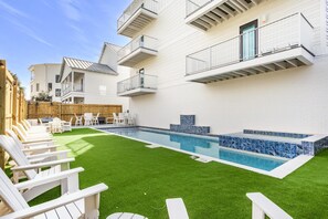 A modern apartment complex with a swimming pool, outdoor seating, and a wooden fence.