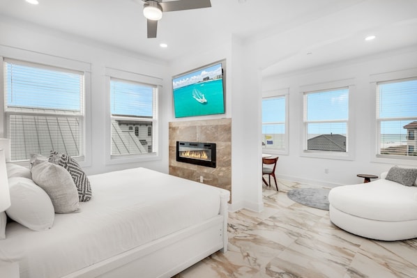 A modern living room with a fireplace, a large TV mounted on the wall, and a view of the ocean through large windows.