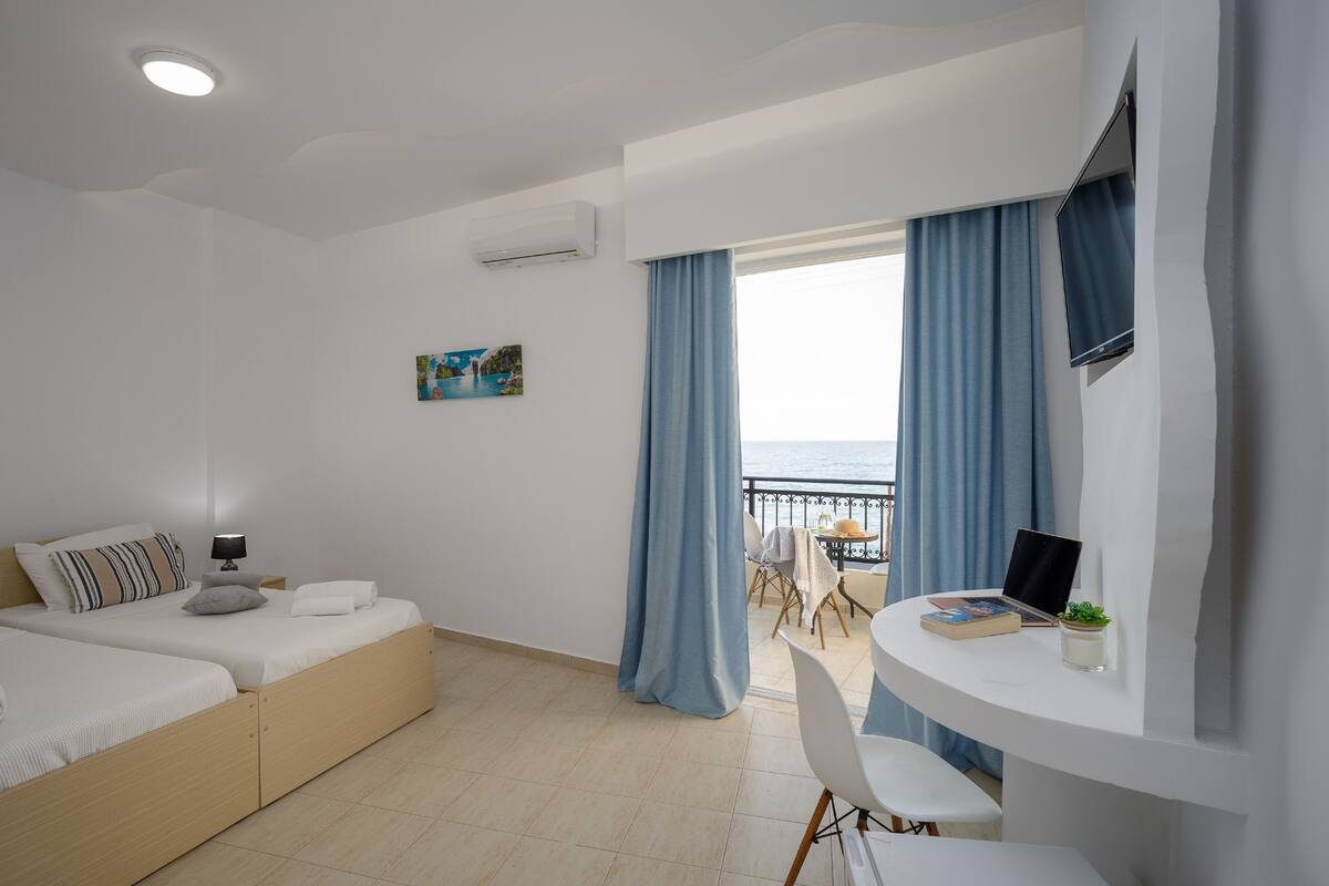 Een moderne slaapkamer met een bed, nachtkastje en uitzicht op zee door grote ramen.