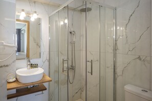 Un baño moderno con lavamanos de mármol, ducha con mampara de vidrio y un inodoro.