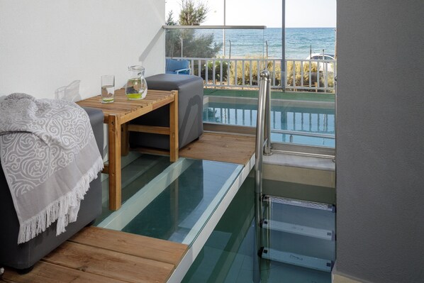 Un balcón con piso de vidrio, una mesa de madera, un sofá gris y vistas al mar.