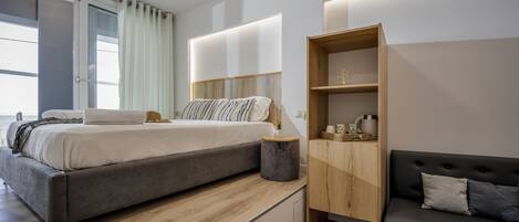 Un dormitorio moderno con una cama, una mesita de madera, un sofá negro y un armario empotrado de madera.