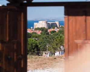Vista a través de una puerta de madera de un pueblo costero con una imponente construcción que recuerda a un castillo al fondo.