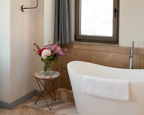 Un baño con una bañera, una mesita redonda pequeña con un florero y una ventana con cortinas.