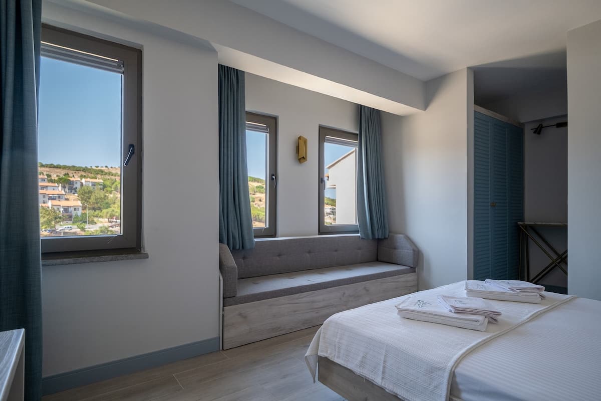 A bedroom with a large window, a built-in bench, and a bed with neatly folded towels.