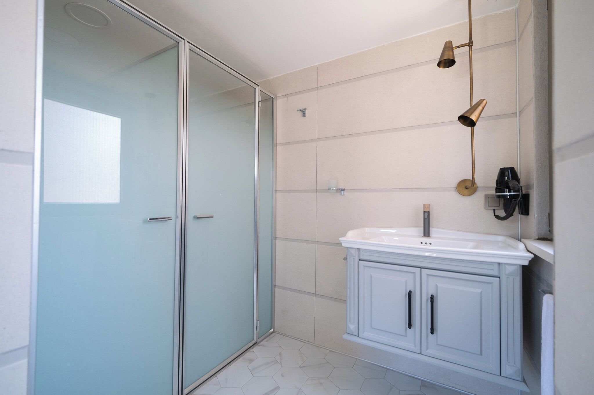 A modern bathroom with a glass shower enclosure, a white sink, and a wall-mounted light fixture.