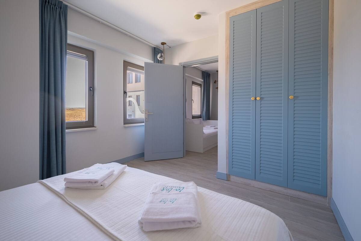 A bedroom with a bed, two towels, a wardrobe, and a window.